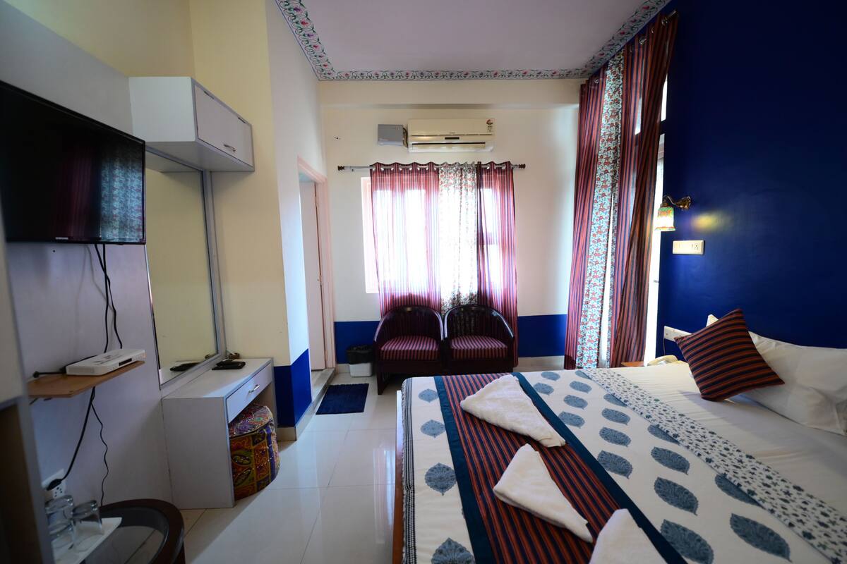 Habitación de hotel con cama, escritorio, silla, aire acondicionado y ventana con cortinas.