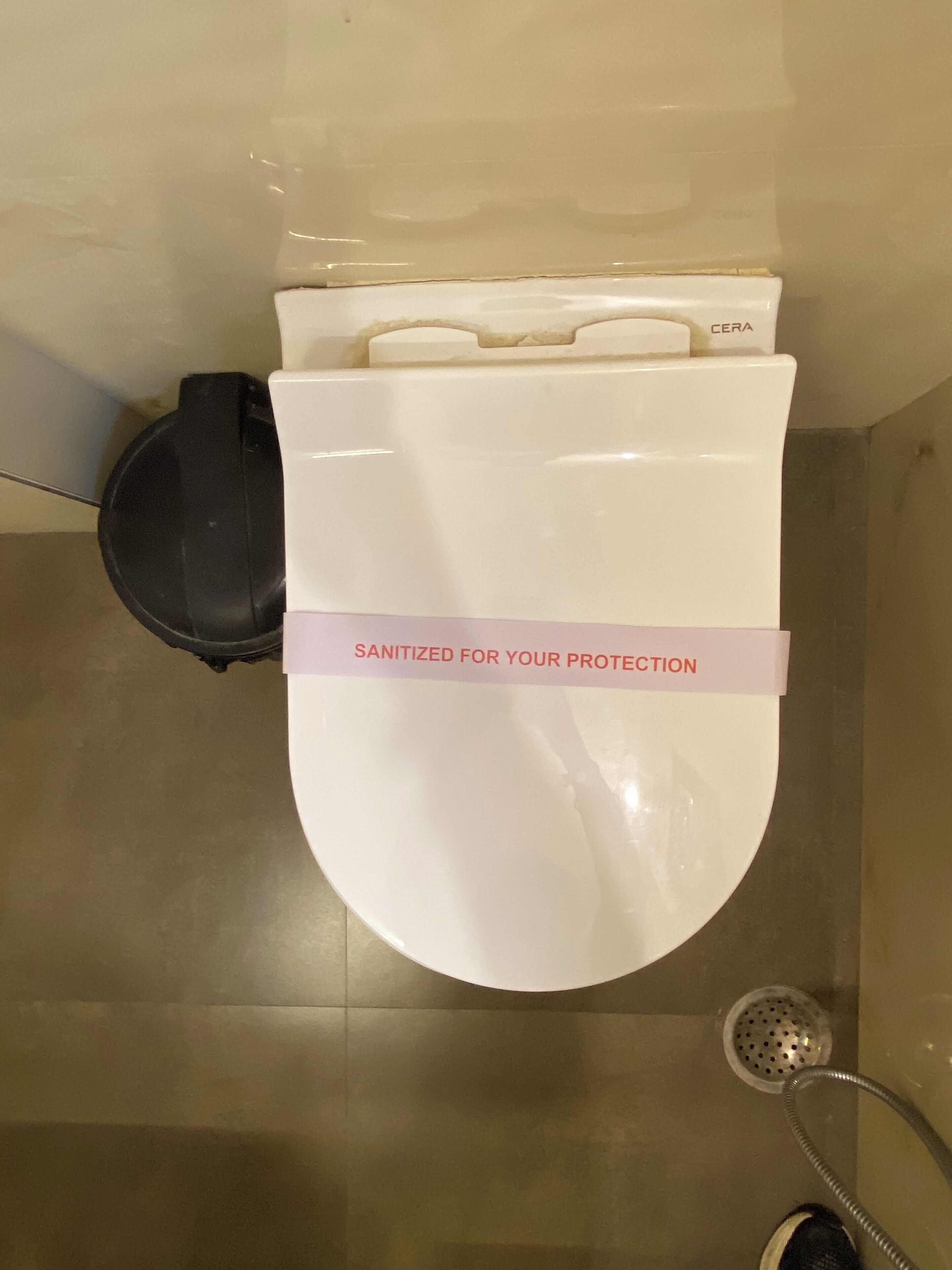 A toilet with a white seat and lid, a black bidet attachment, and a pink sign stating "SANITIZED FOR YOUR PROTECTION".