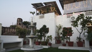 A courtyard with a fountain, potted plants, and a white wall with string lights. - Chitra Katha - A Story Per Stay (Jaipur)