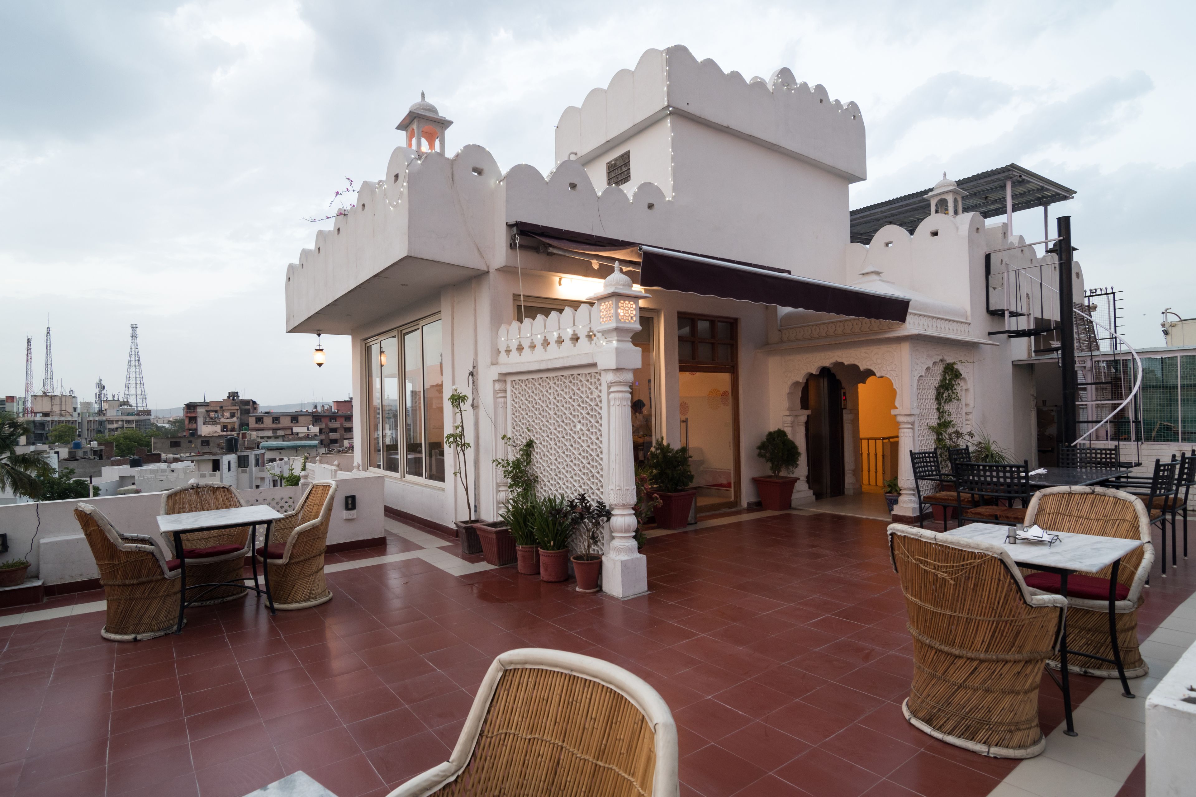 A rooftop terrace with wicker furniture, potted plants, and a view of the cityscape.