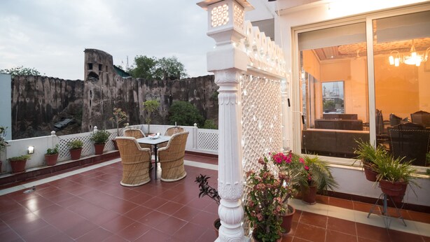 A terrace with wicker furniture, potted plants, and a view of a rocky cliff. - Chitra Katha - A Story Per Stay (Jaipur)