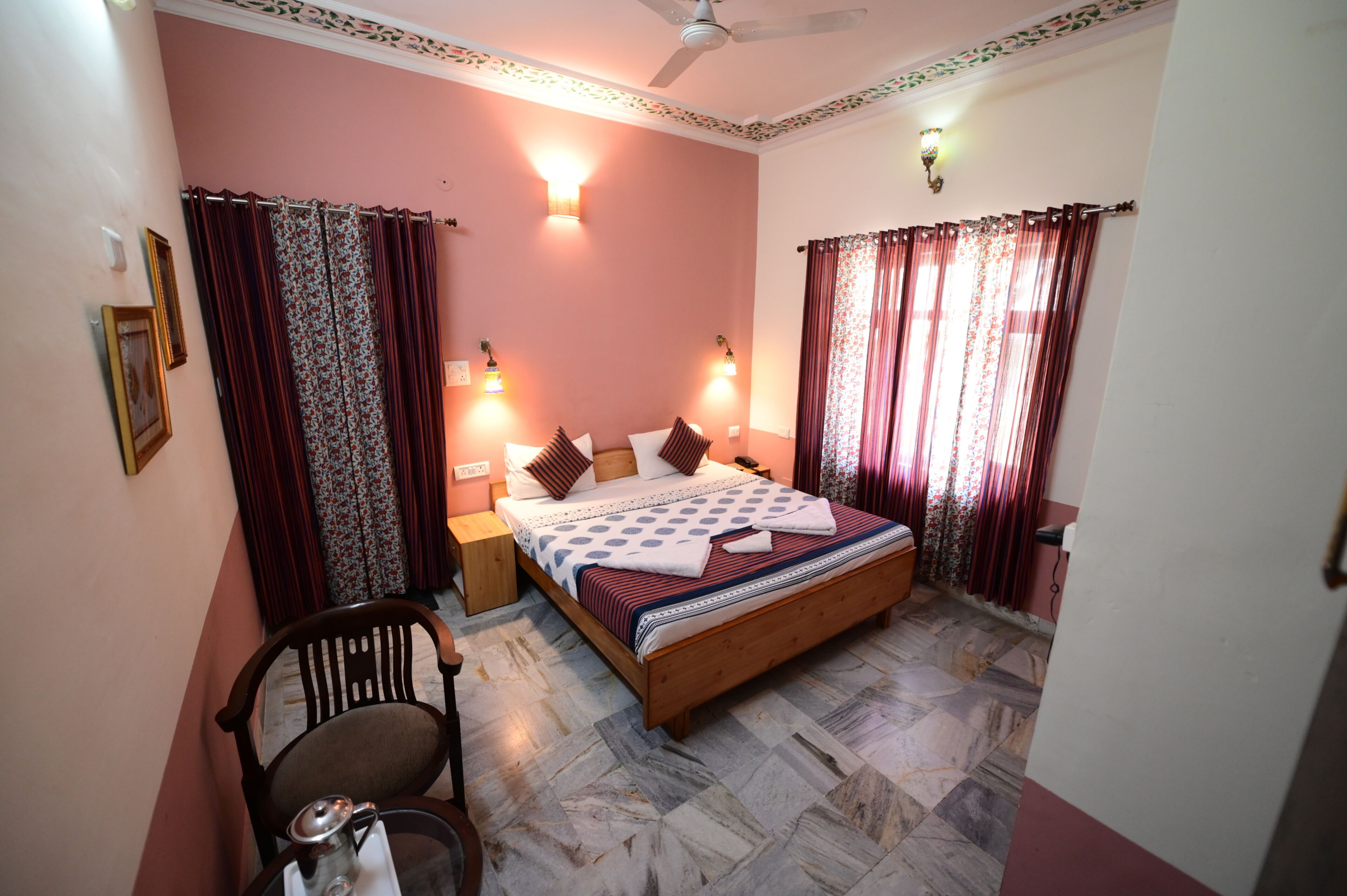 A bedroom with a wooden bed, patterned curtains, a ceiling fan, and wall-mounted lights.