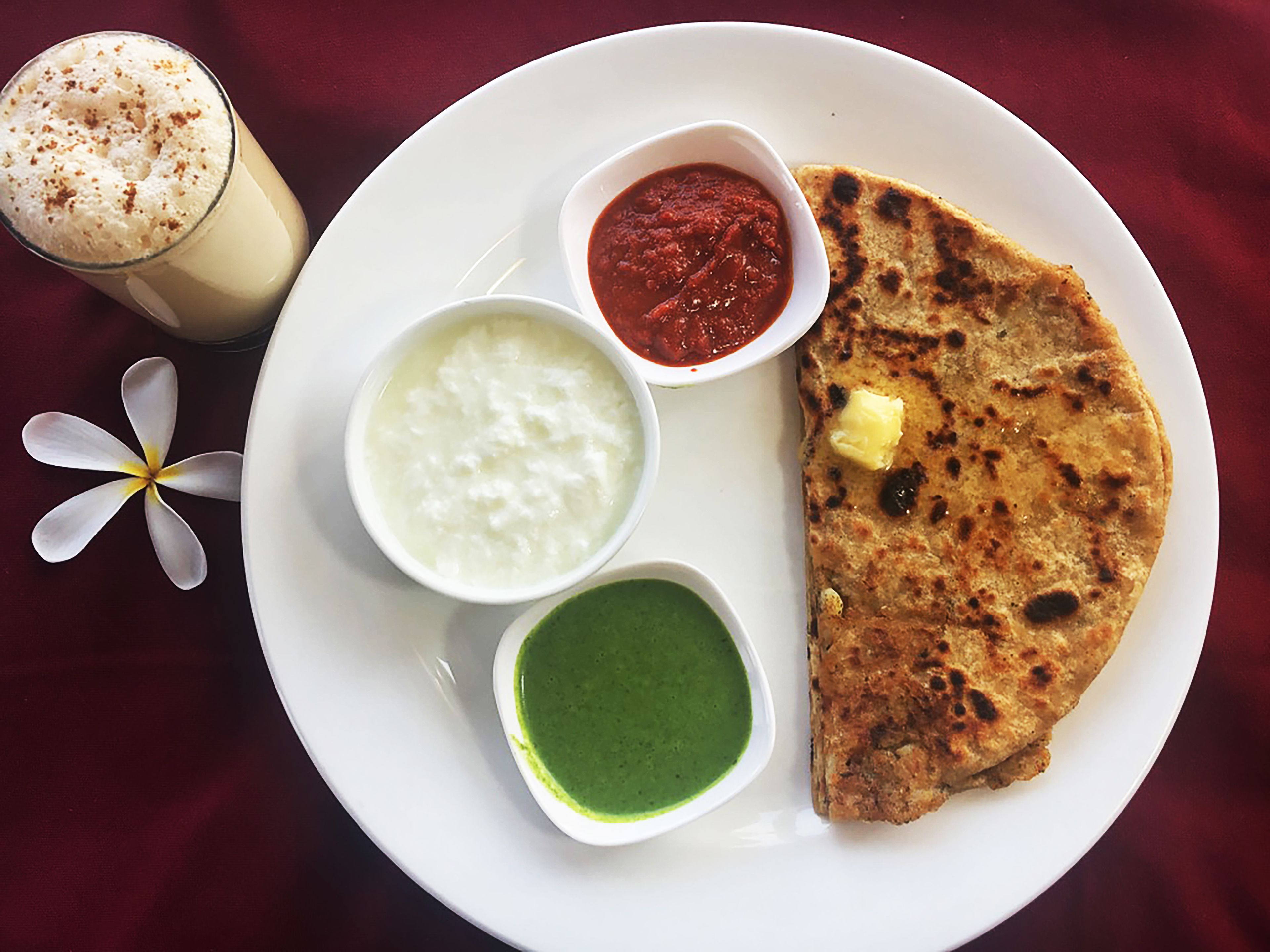 A plate with a flatbread, two types of chutney, a creamy dish, and a green sauce.