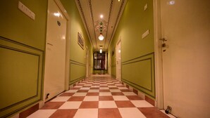 A hotel hallway with green walls, checkered floor, and a decorative ceiling light. - Chitra Katha - A Story Per Stay (Jaipur)