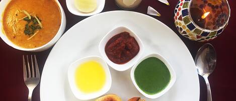 A table with a plate of food including soup, bread, and condiments.