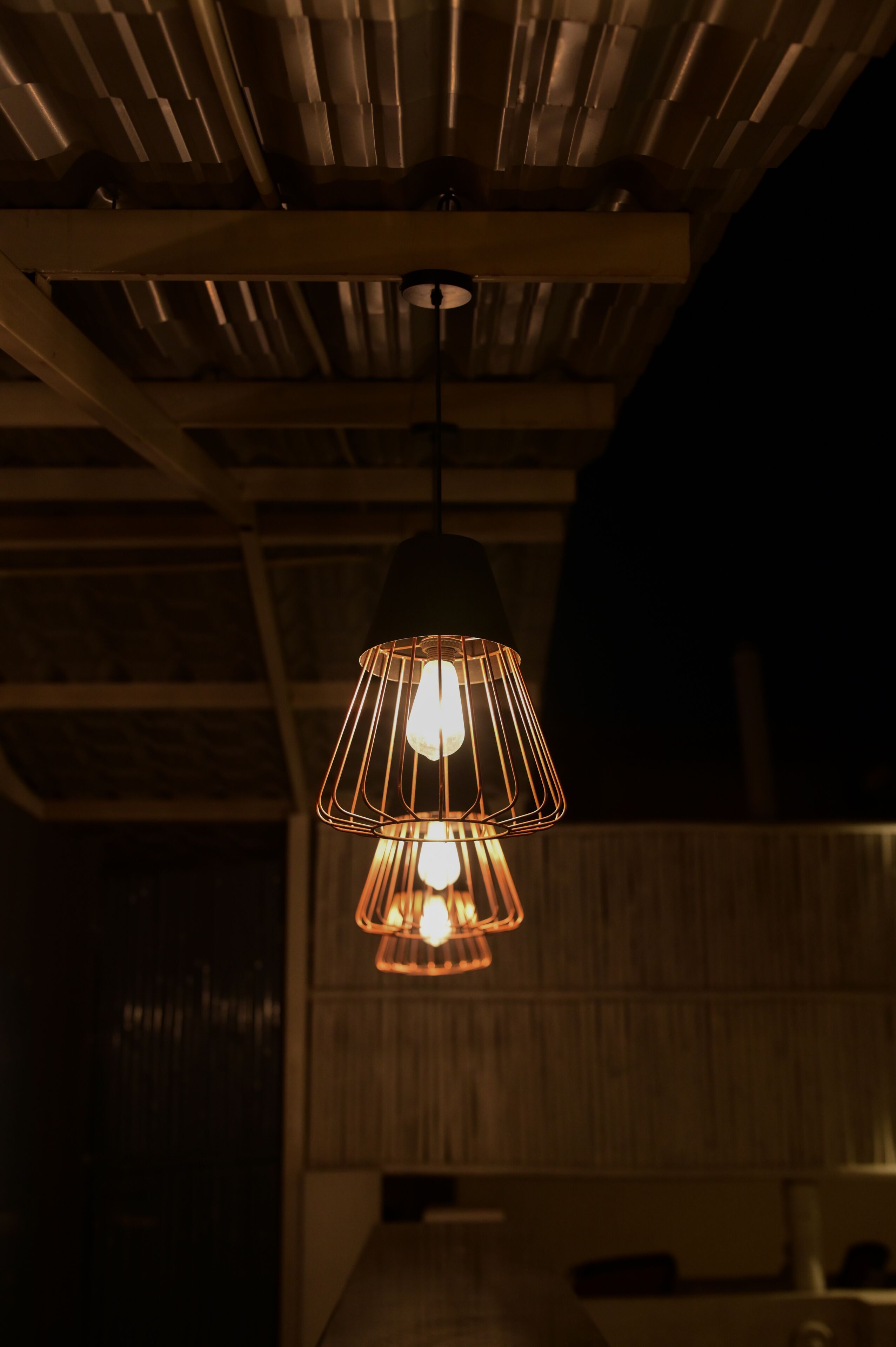 A pendant light fixture with a geometric design hanging from a ceiling with exposed wooden beams.