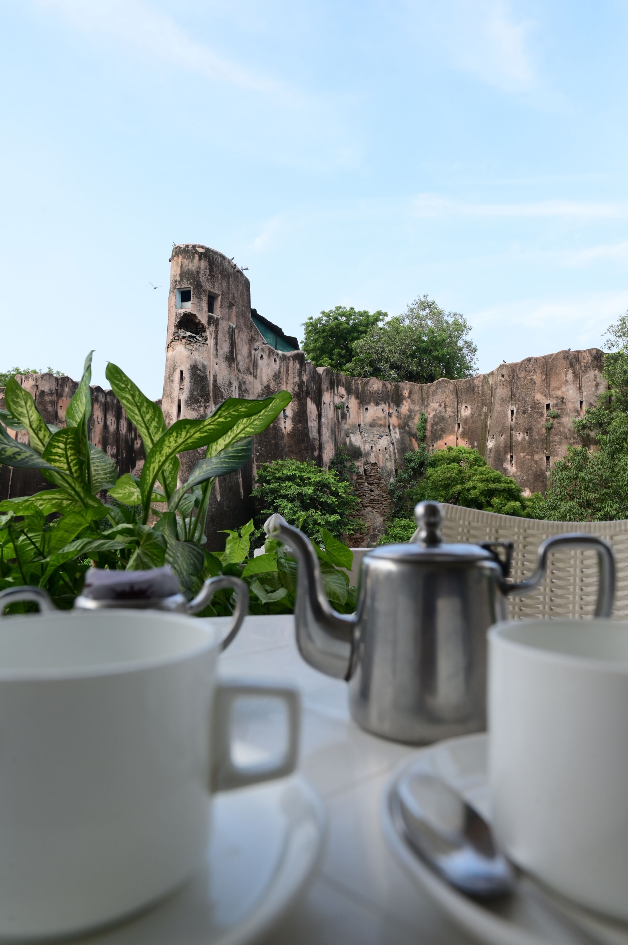 A table with a teapot and cups, a view of a historic fort wall, and lush greenery.