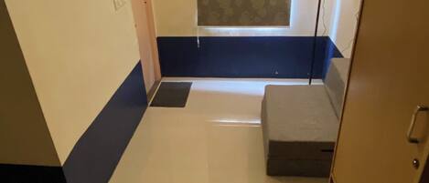 Ein Hotelzimmer mit Bett, Schreibtisch, Stuhl, Kleiderschrank, Deckenventilator und einem Fenster mit gemusterten Vorhängen.