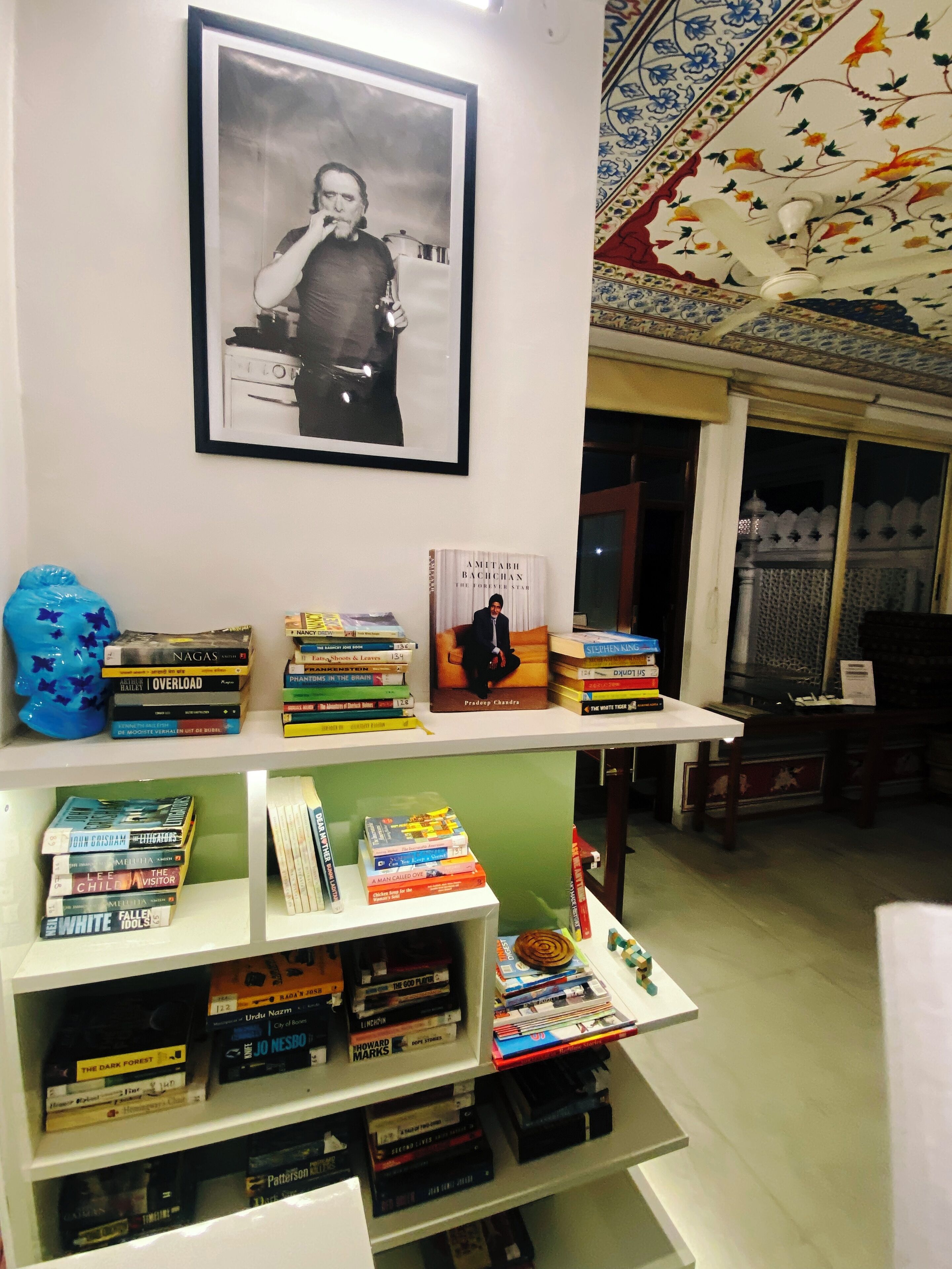 A bookshelf with various books, a framed black and white photograph, and a decorative ceiling.