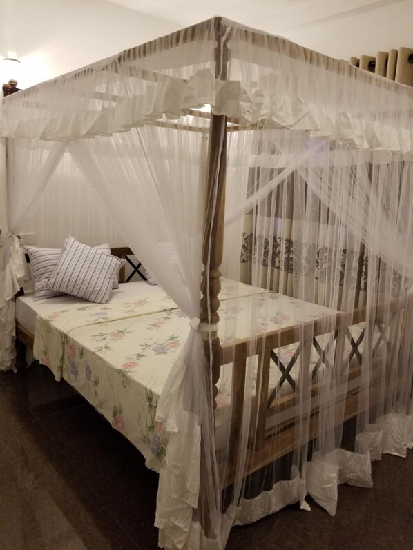 A four-poster canopy bed with a floral bedspread and striped pillows. - Coral Palm Villa & Apartments (Unawatuna)