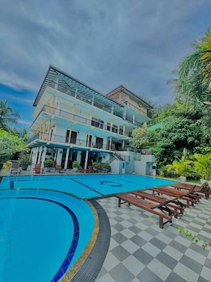 Un hôtel doté d’une piscine, de nombreux balcons et d’une végétation luxuriante.