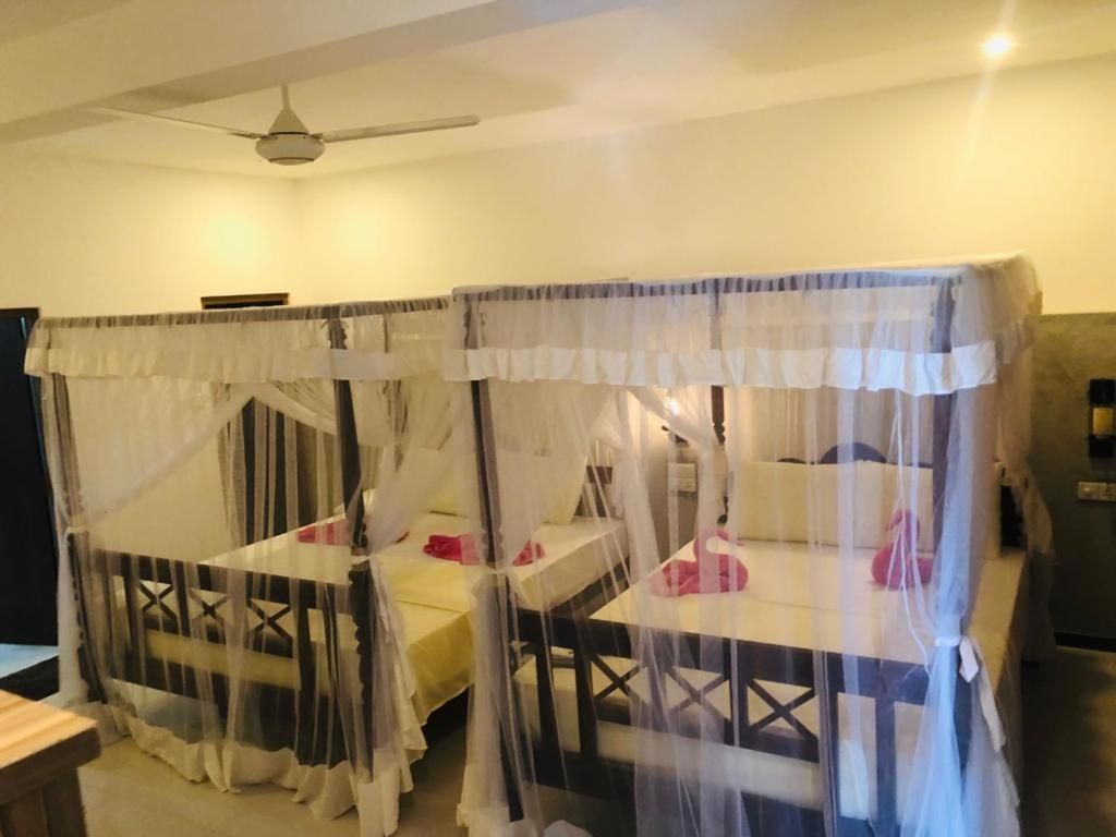 A room with two beds, each covered with a canopy. There is a ceiling fan and a table with chairs.