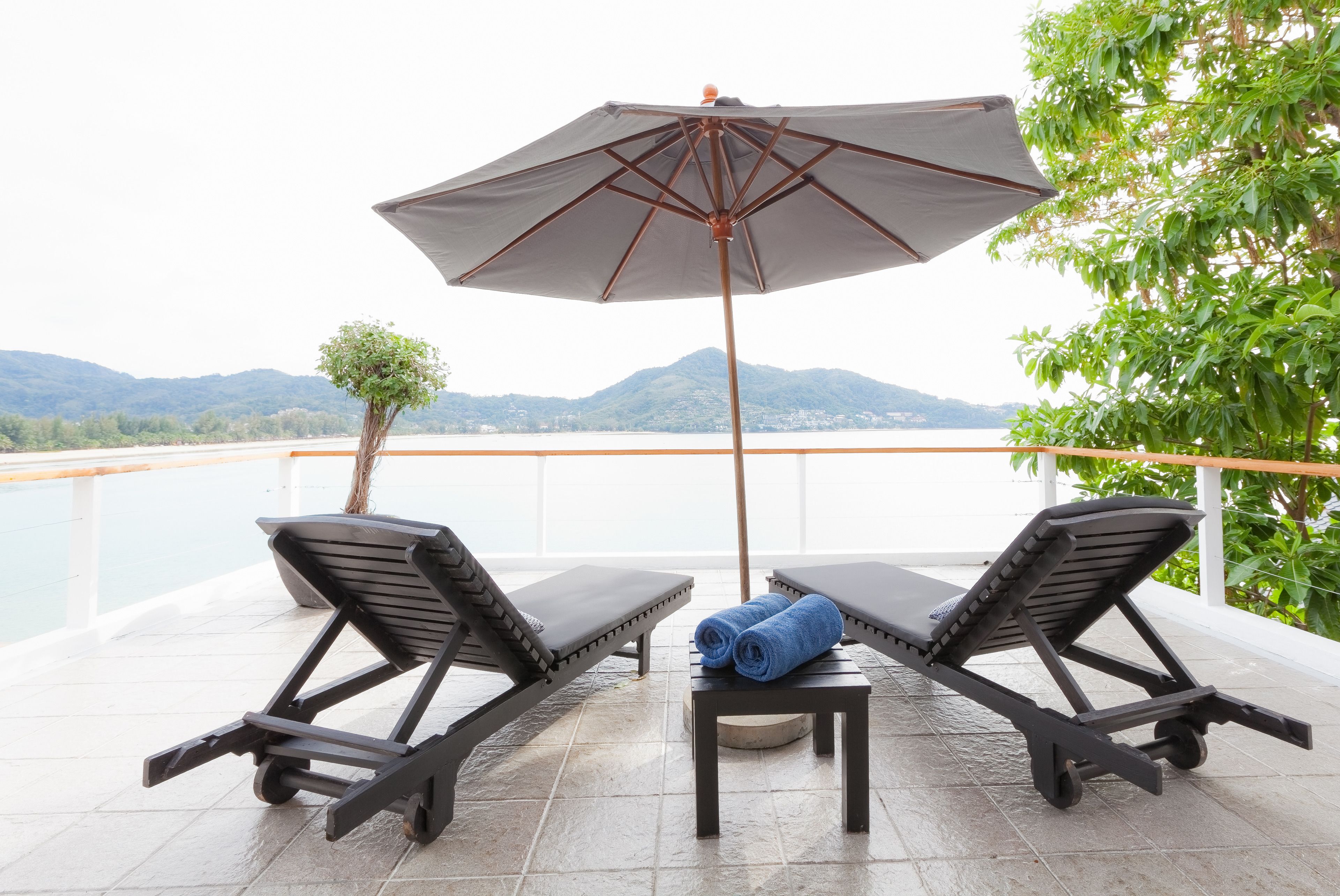 Een balkon met twee ligbedden, een tafel met een opgerolde handdoek, en een grote parasol.