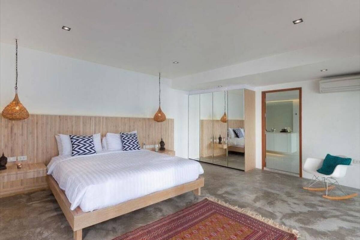 Un dormitorio moderno con una cama de madera, un tapete estampado y una silla blanca.