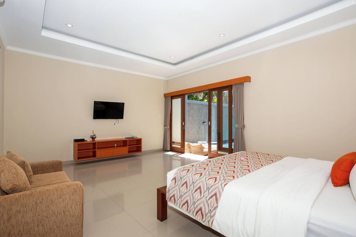 A modern bedroom with a large bed, a sofa, a TV, and a sliding glass door leading to a balcony.