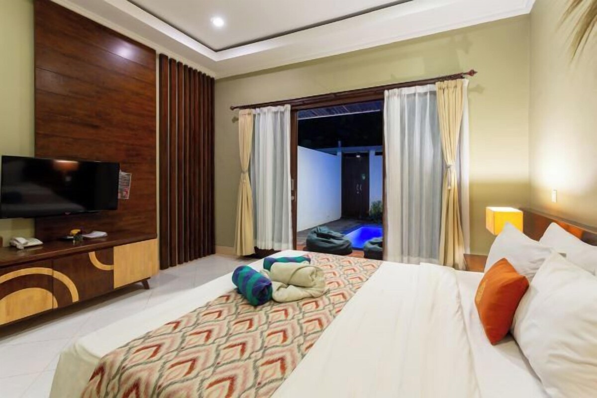 A hotel room with a bed, a TV, a desk, and a view of a pool.