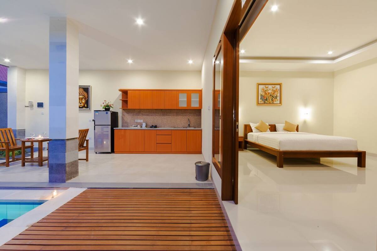 A modern hotel room with a wooden bed, a small kitchen, and a pool area.