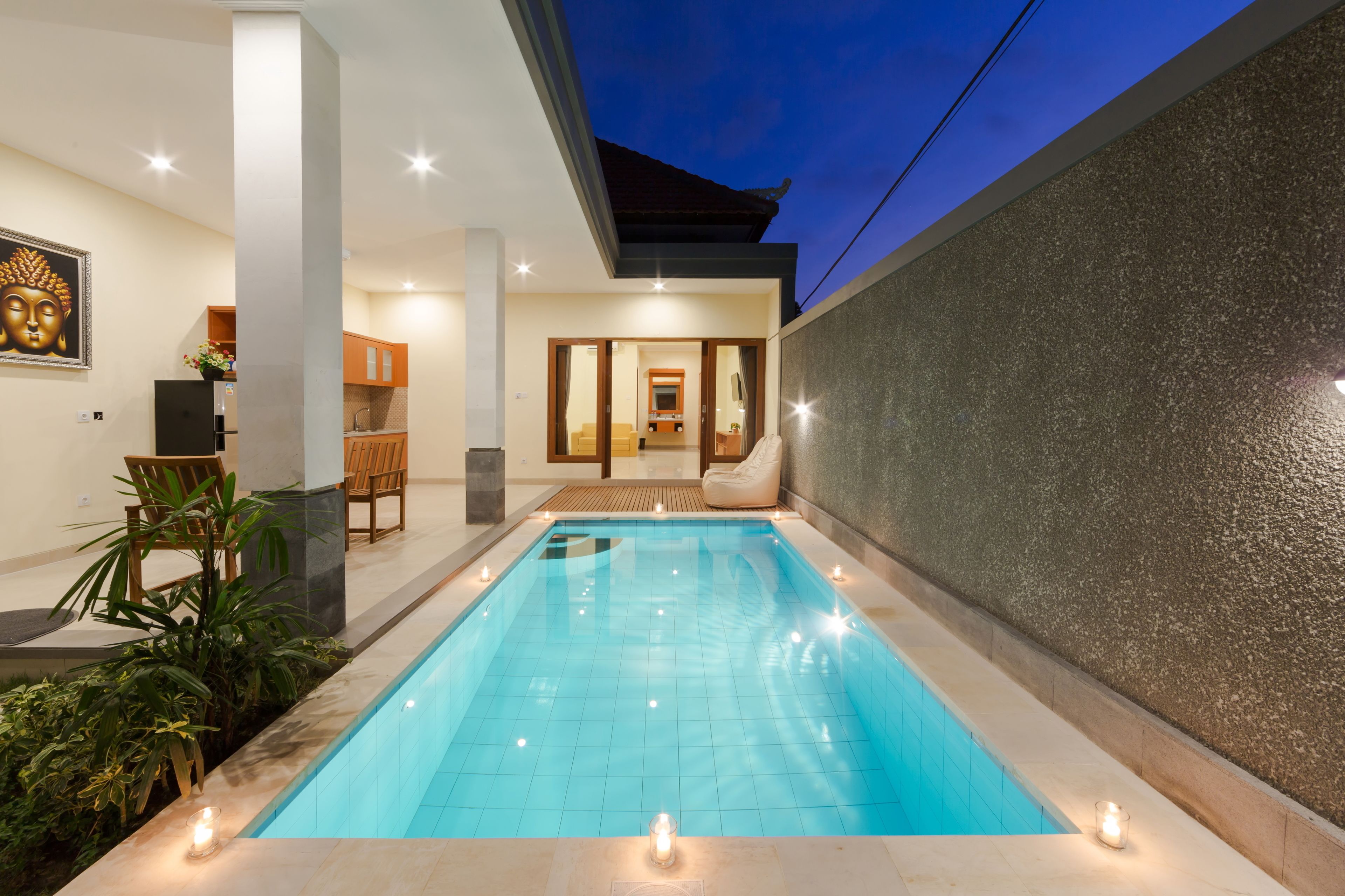 Ein moderner, überdachter Pool mit klarem, blauem Wasser, umgeben von einer gefliesten Promenade und einigen Pflanzen.
