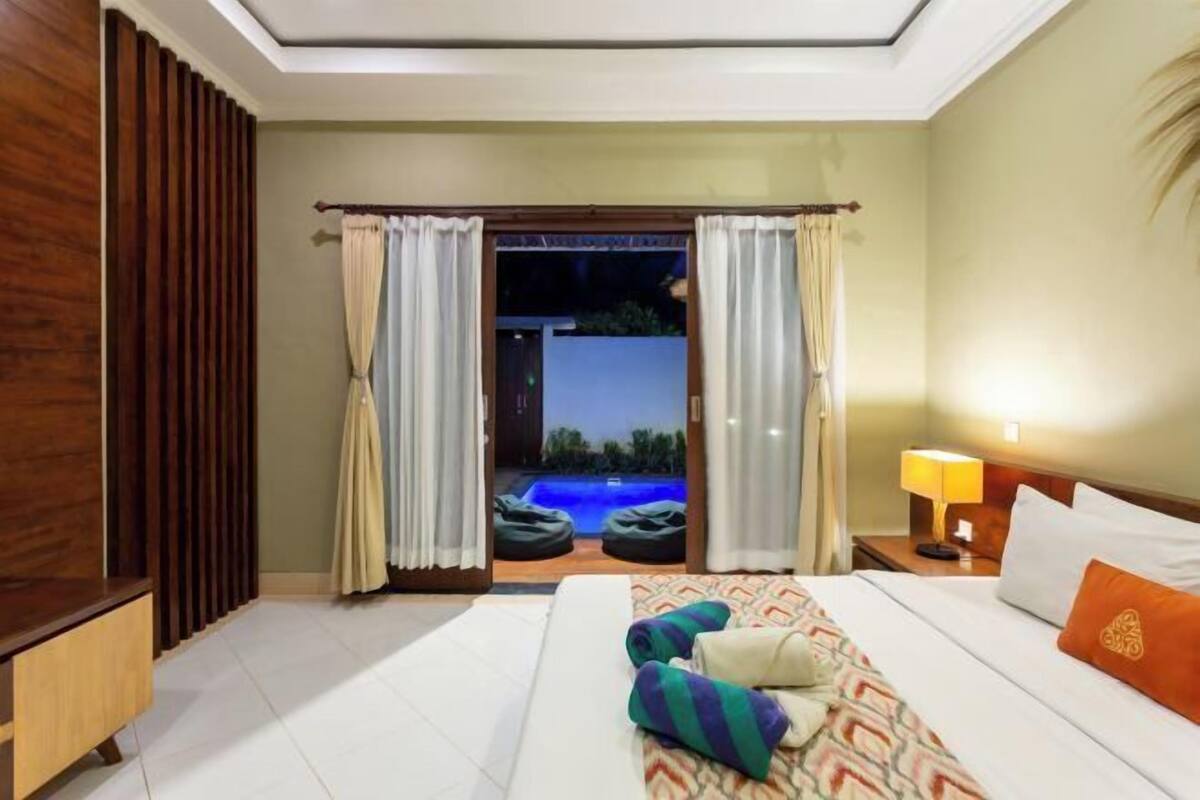 A hotel room with a bed, a nightstand, a lamp, a view of an outdoor pool, and a sliding door.