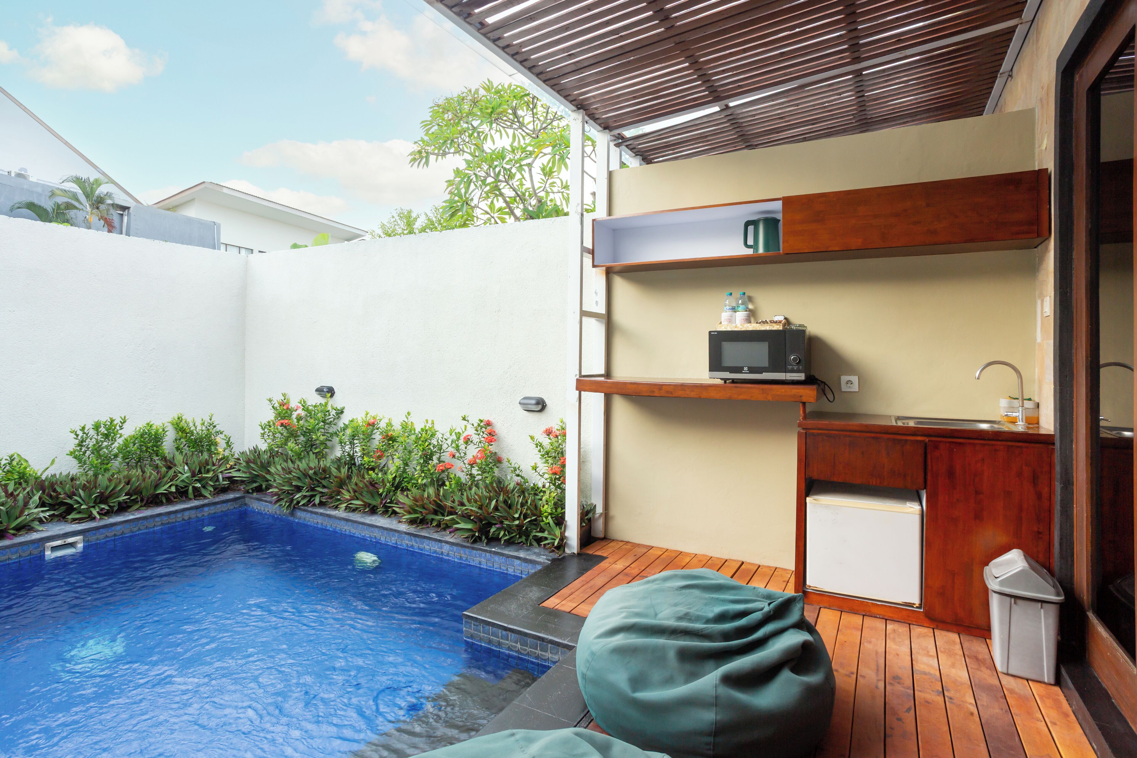 Una piscina con cubierta de madera, una pequeña cocina con microondas y un cubo de basura.
