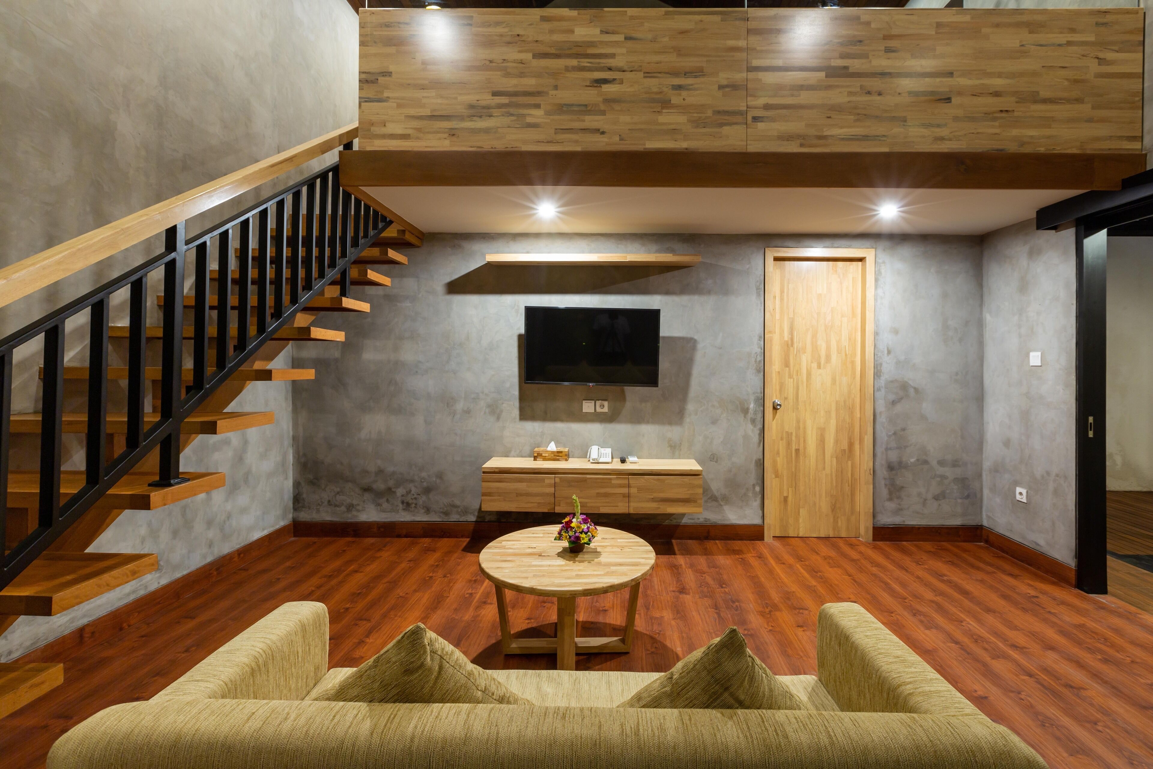 A modern living room with a wooden staircase, a round wooden coffee table, and a sofa.