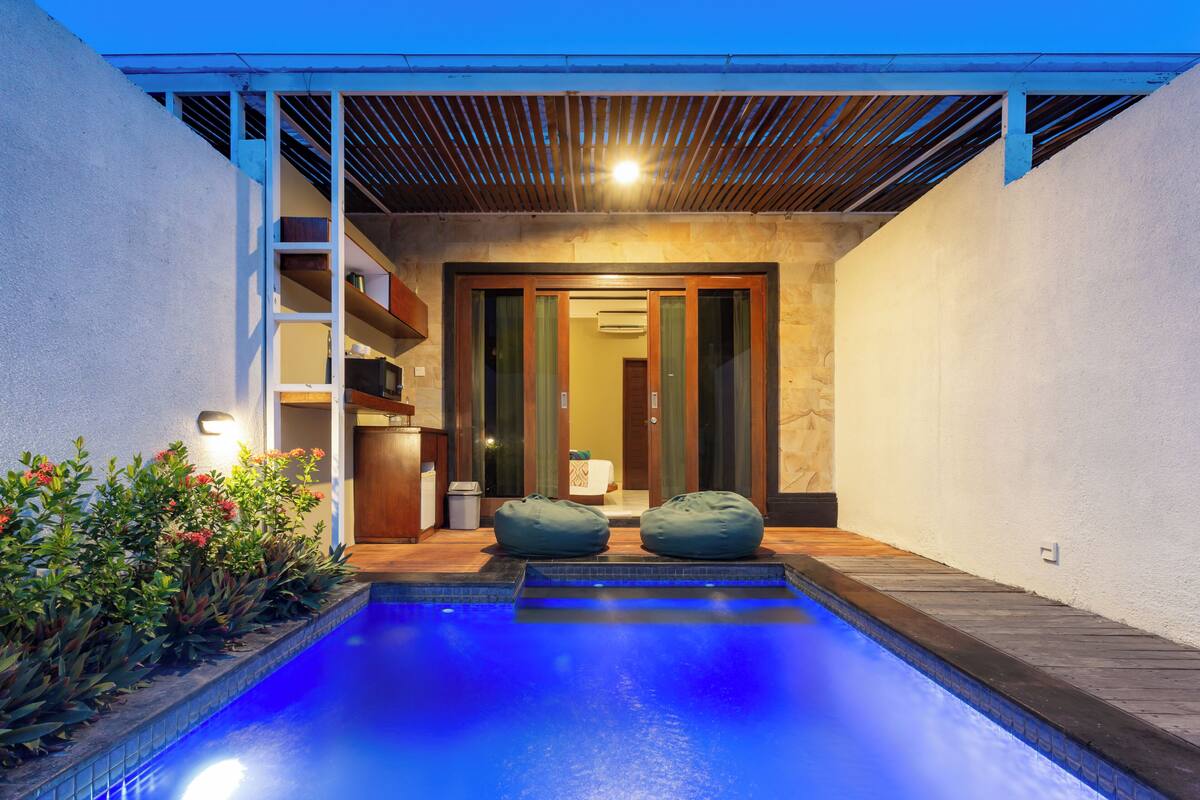 A swimming pool with two bean bags, a wooden deck, and a stone wall.