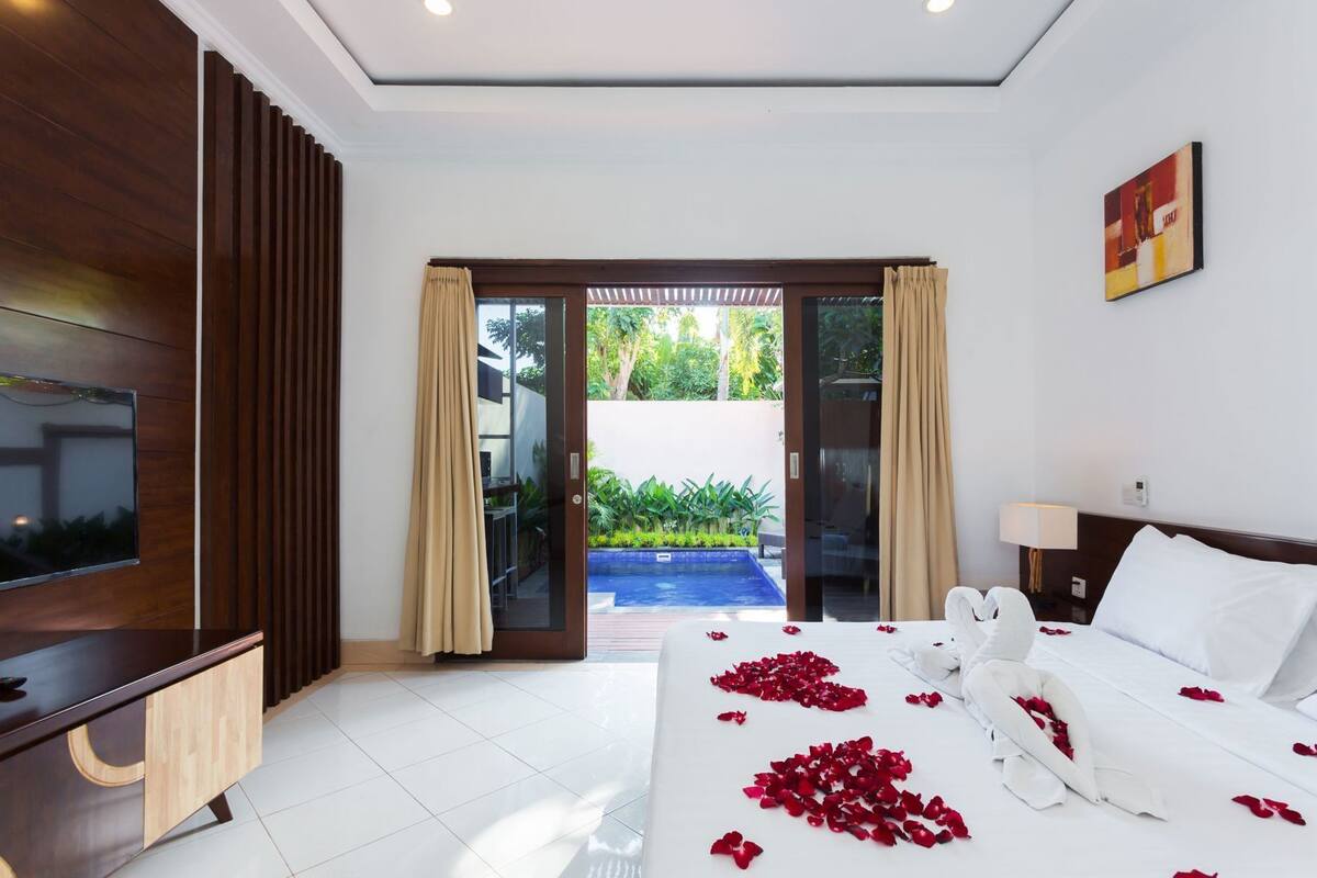 A hotel room with a bed, a TV, a desk, and a view of a pool.