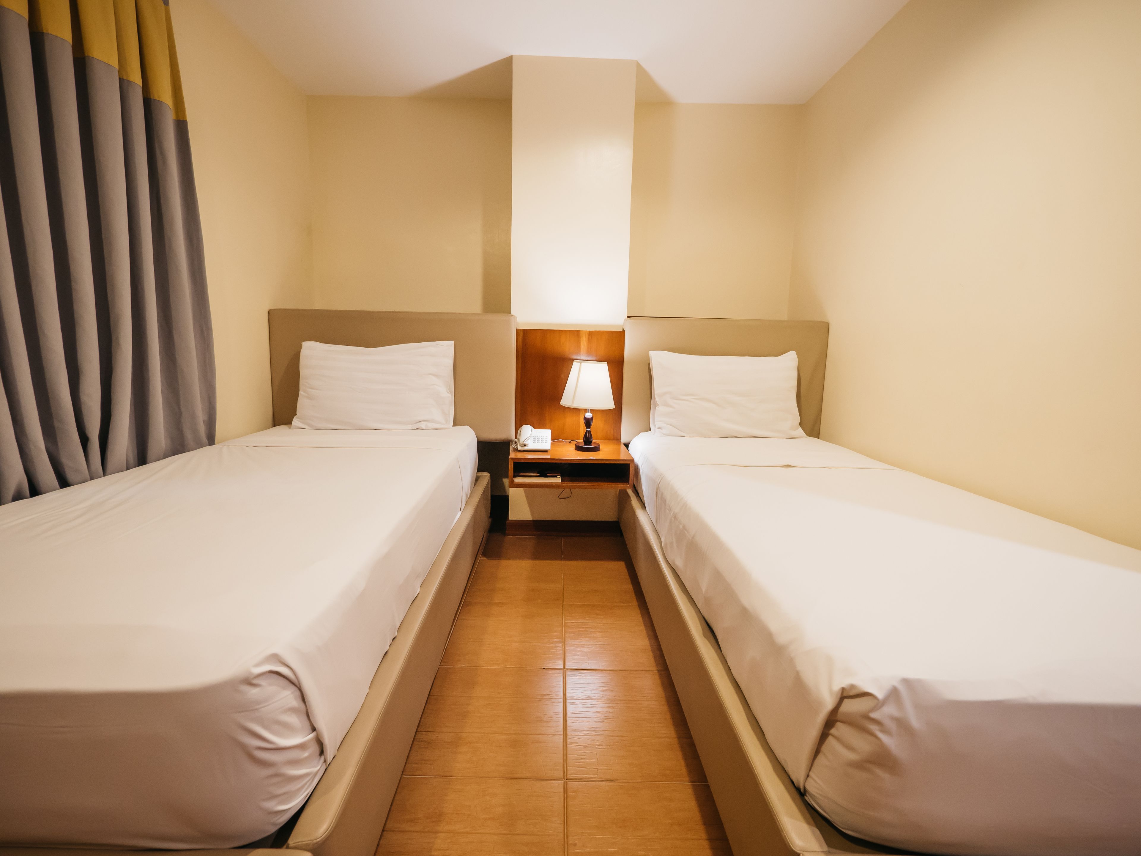 Una habitación de hotel con dos camas individuales, una mesita de noche con lámpara y teléfono.