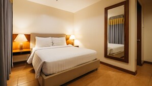 Une chambre d’hôtel avec un grand lit, deux tables de chevet avec des lampes, un miroir et une porte.