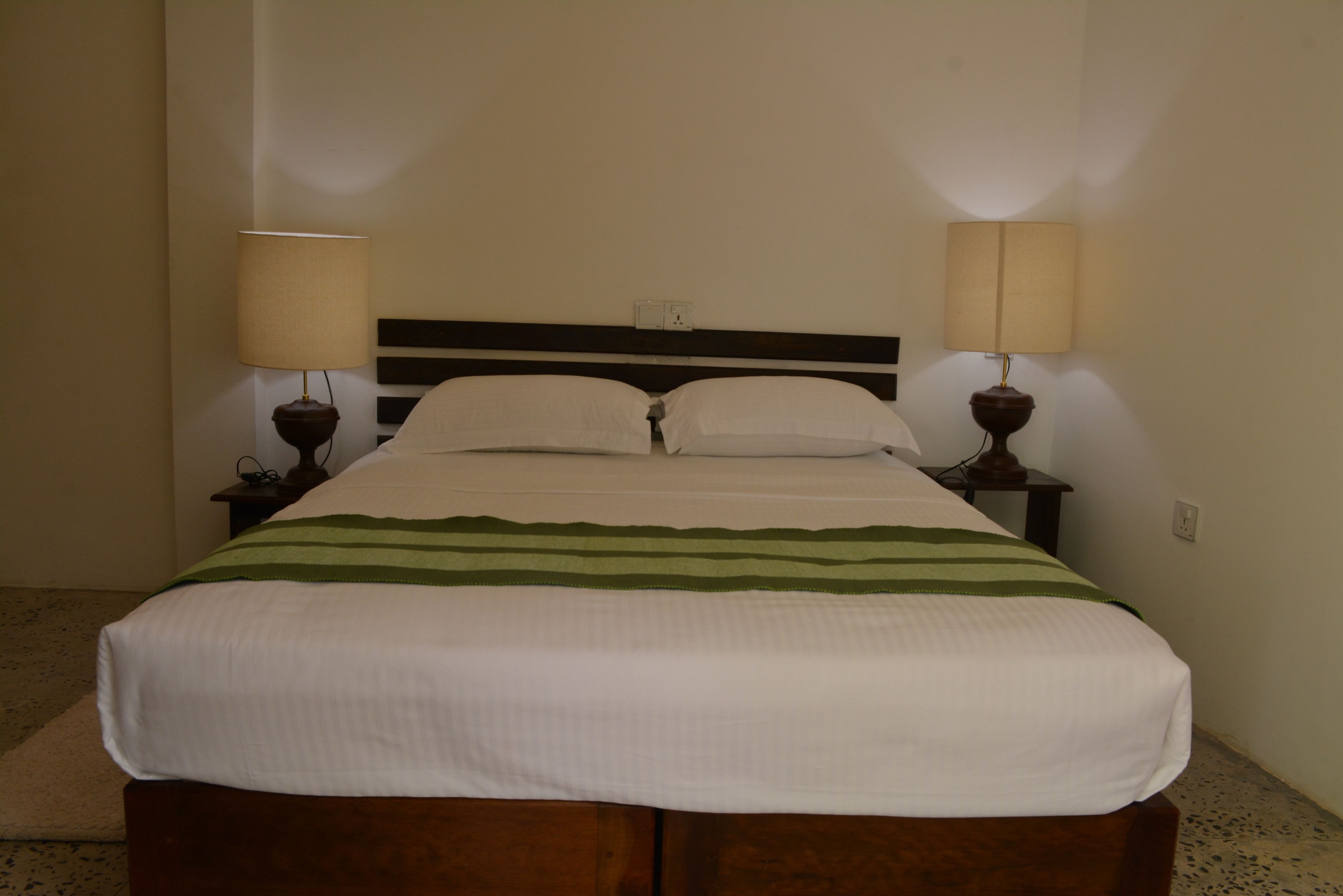 A neatly made bed with a white and green striped blanket, two bedside lamps, and a wooden headboard.