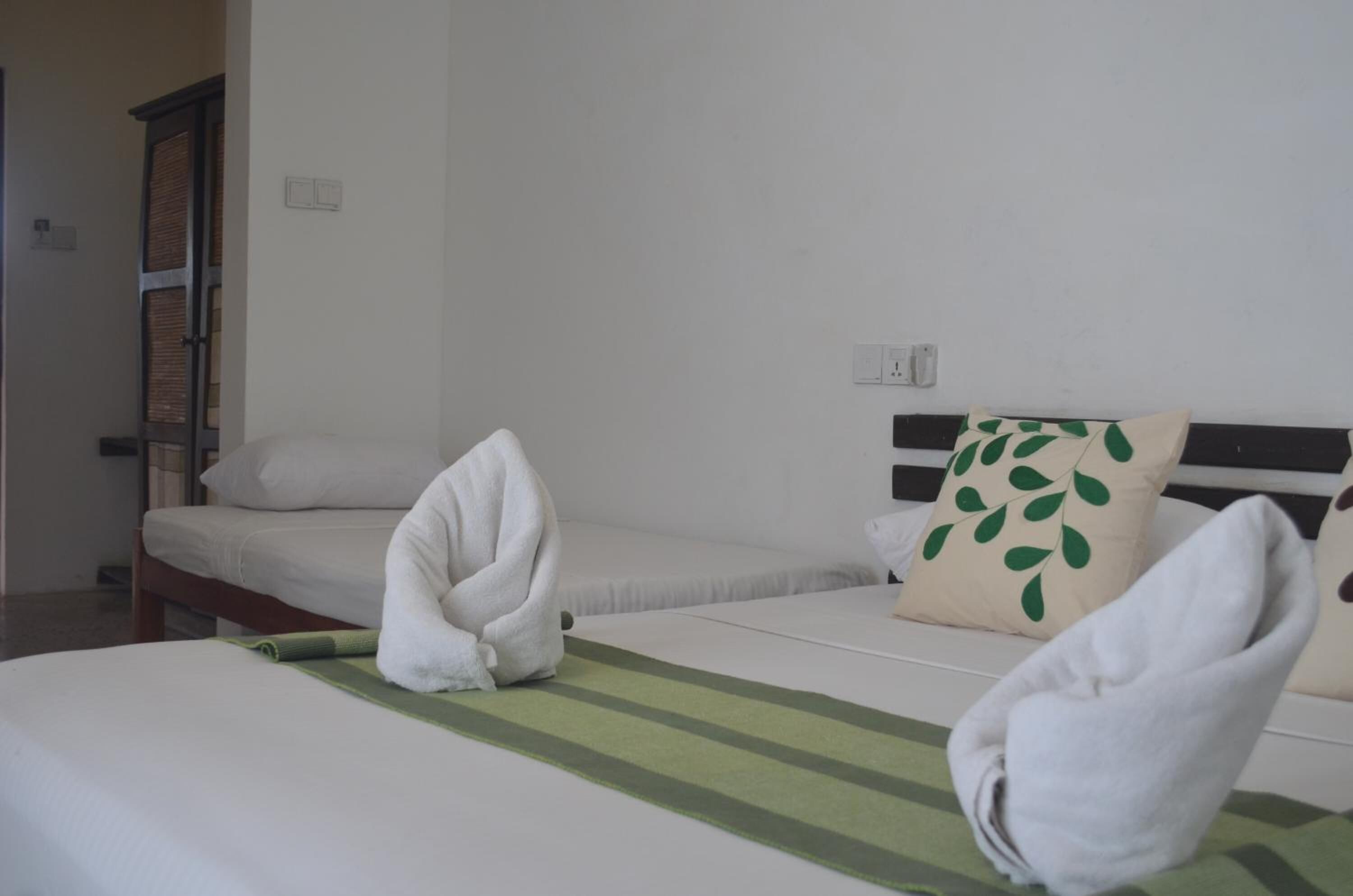 A hotel room with two beds, a wooden wardrobe, and a green-striped bedspread.