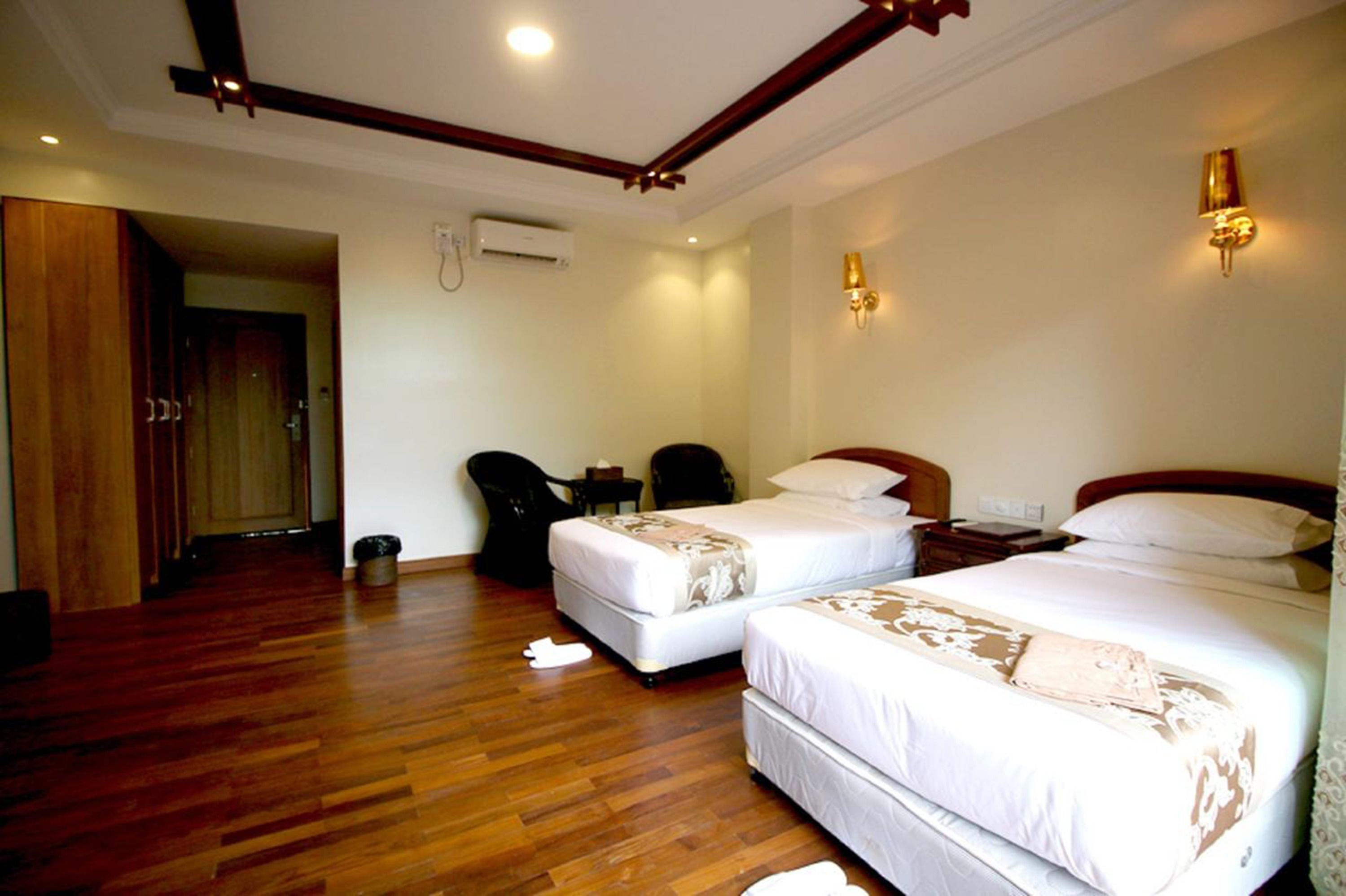 A hotel room with two beds, wooden flooring, a desk, a chair, and a small table.