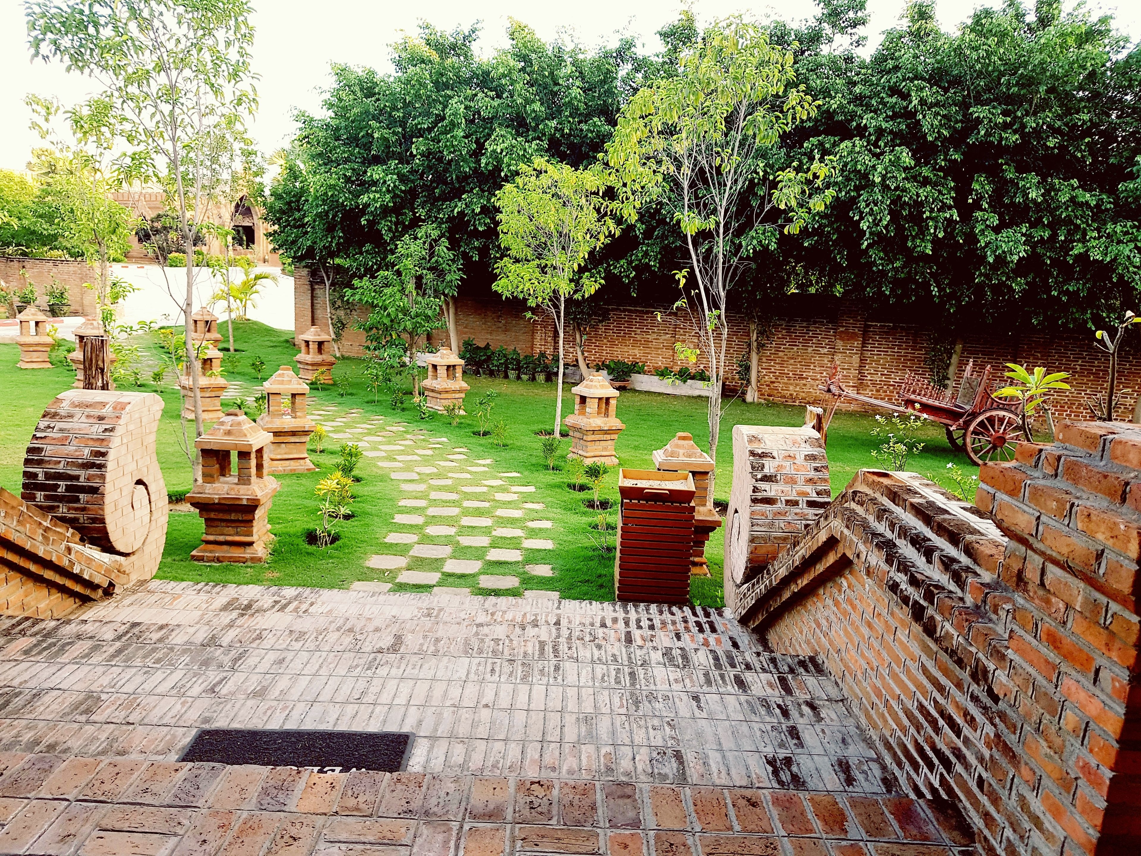 Un patio con un sendero a cuadros, construcciones de ladrillo y follaje.