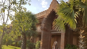 A traditional building with a brick facade, a balcony, and a well-maintained garden with palm trees and shrubs. - Famous Hotel Bagan (Nyaung-U)