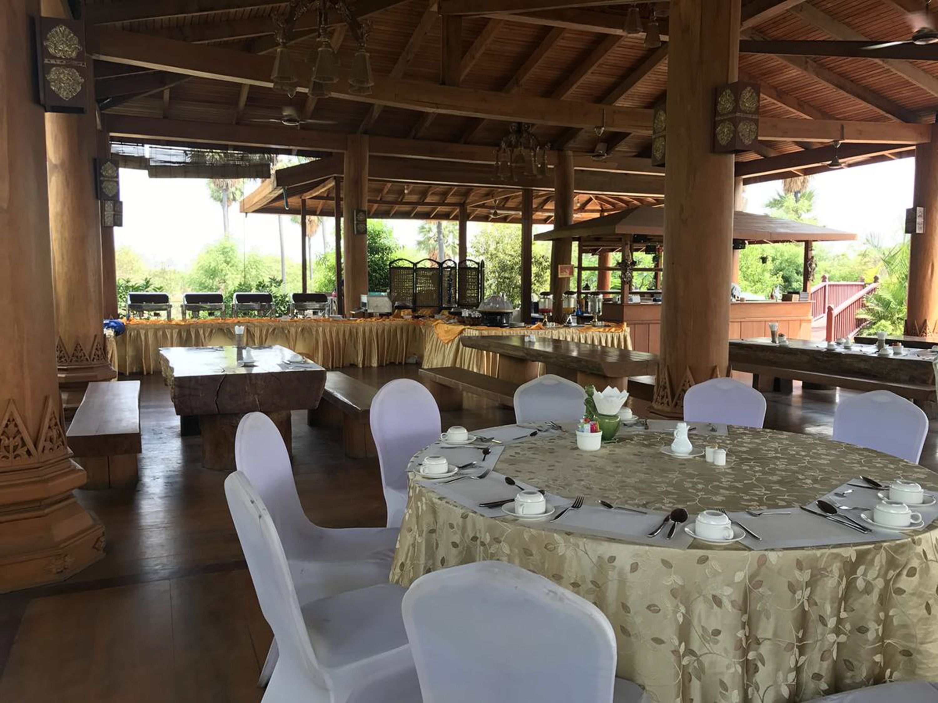 A covered outdoor dining area with tables set for a meal, surrounded by columns and a wooden ceiling.