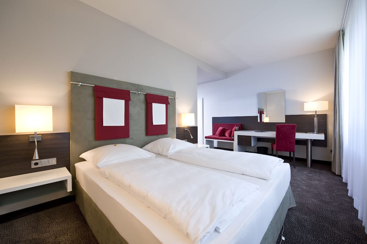 Habitación de hotel con una cama grande, un escritorio y una silla. Hay dos mesitas de noche con lámparas.