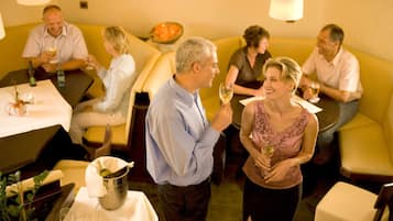 Un groupe de personnes est réuni dans un restaurant, autour de tables et de chaises, et une bouteille de champagne est posée sur l’une d’elles.