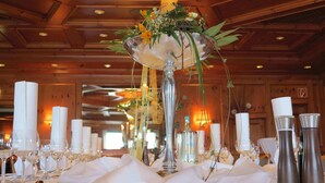Una mesa de banquete con manteles blancos, candelabros de plata y un arreglo floral central.