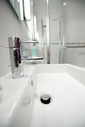 Un baño moderno con lavamanos blanco, grifo cromado y cabina de ducha de vidrio.