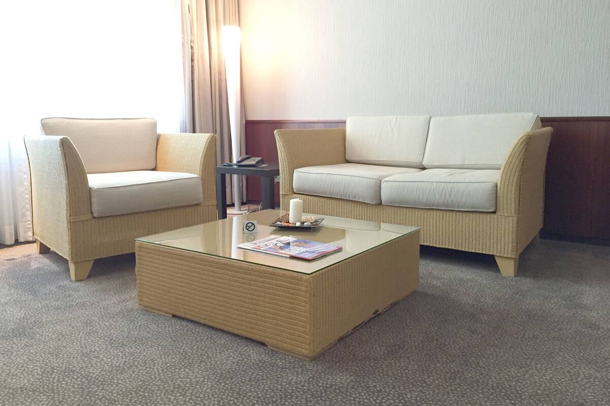 Habitación de hotel con dos sofás color beige, una mesa de centro de vidrio y una mesita auxiliar con un teléfono y velas.
