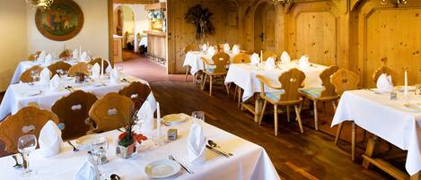 Un restaurante con varias mesas dispuestas para comer, sillas de madera y lámparas verdes colgantes.