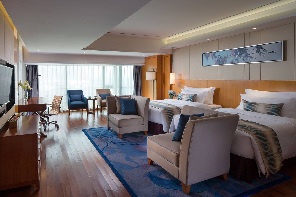 A hotel room with a large bed, two armchairs, a sofa, a desk, and a TV.