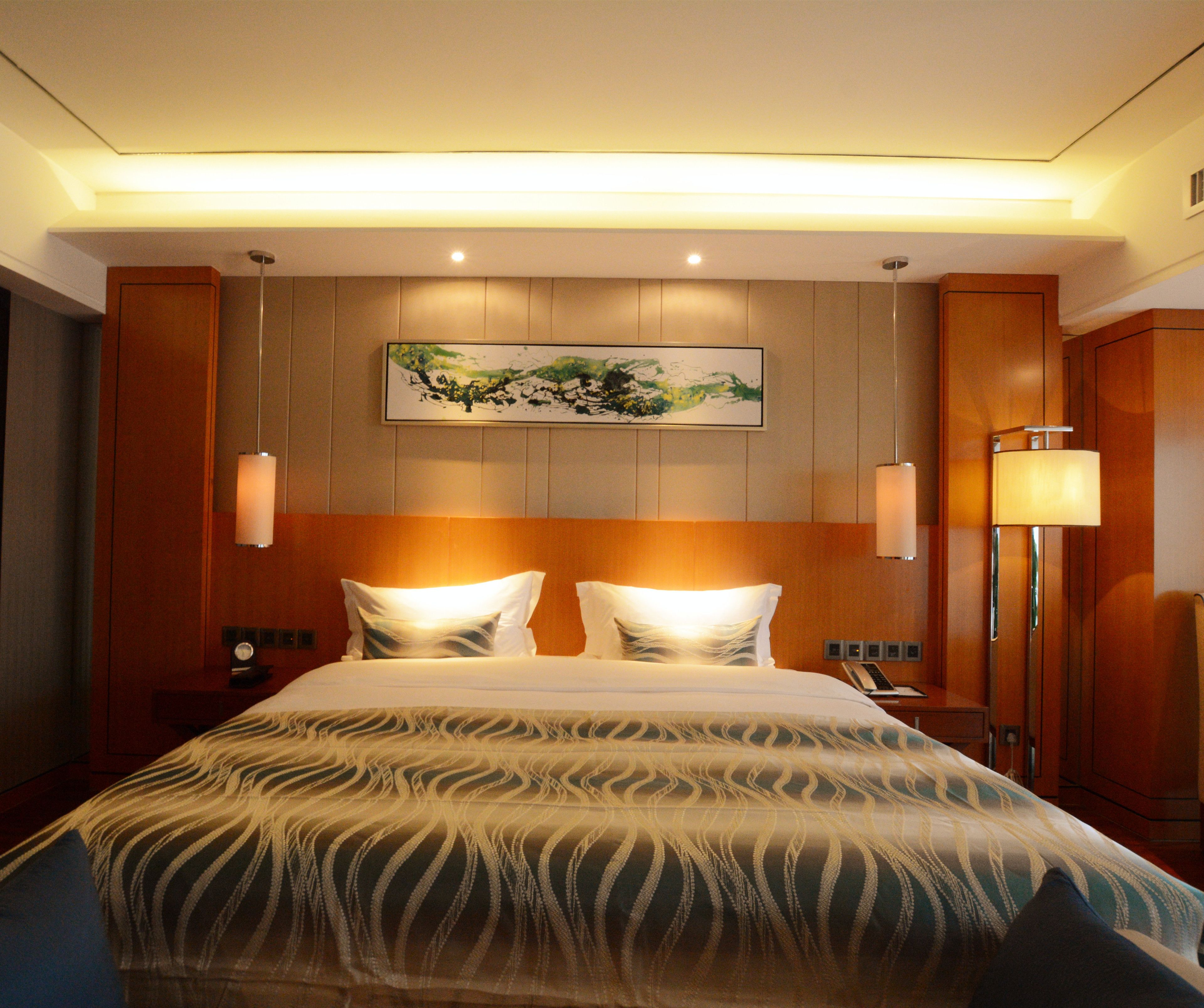 Ein Hotelzimmer mit einem großen Bett, einem Vorhang mit einem Gemälde, einem Nachttisch, einer Lampe und einem an der Wand befestigten Telefon.