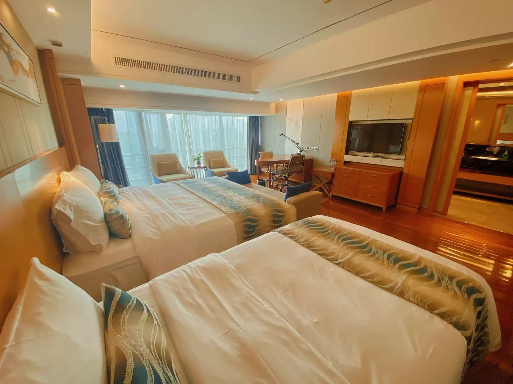A hotel room with two beds, a desk, a TV, and a dining area.