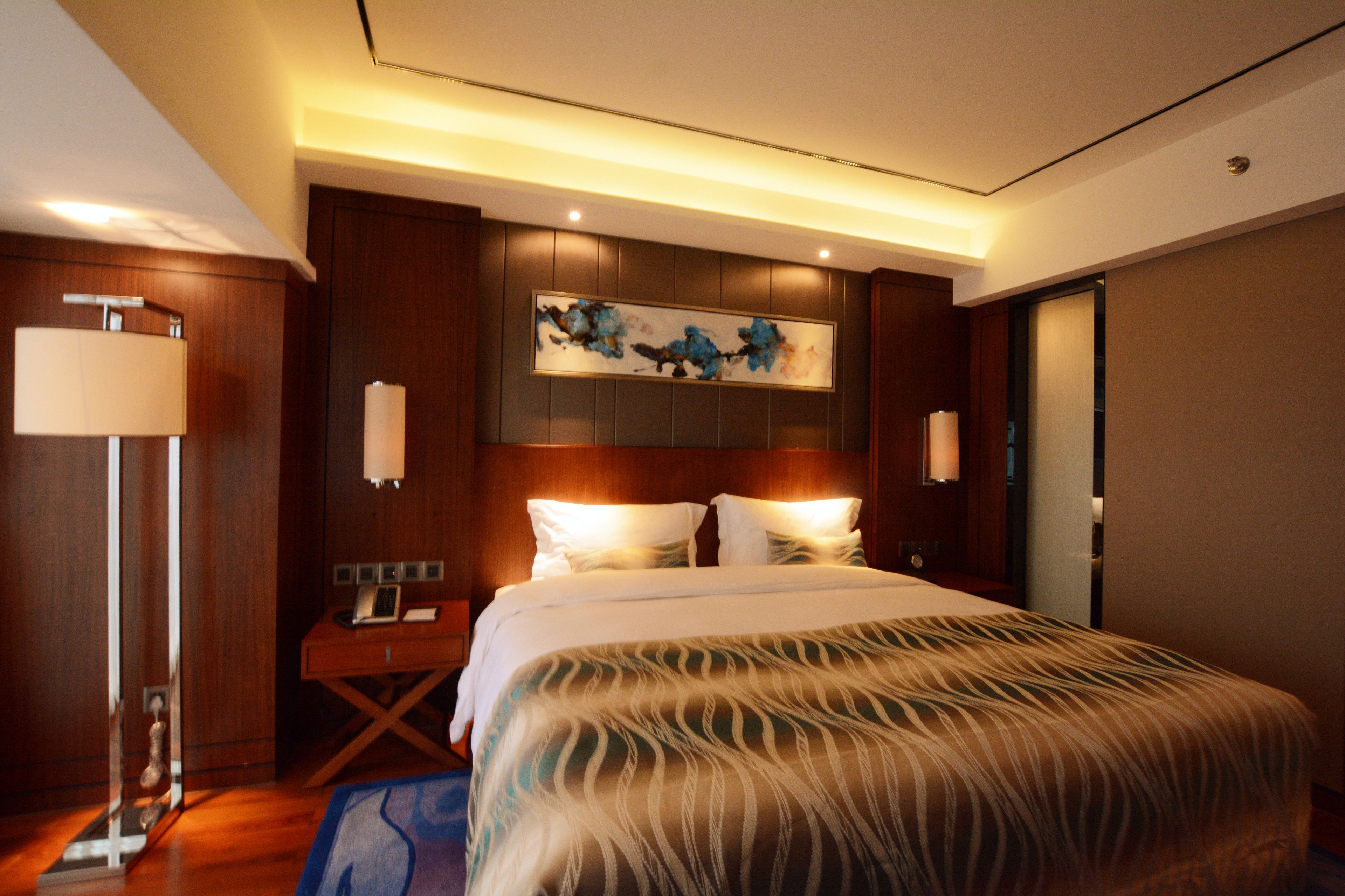 Una habitación de hotel con una cama grande, una mesita de noche, una lámpara y un cuadro en la pared.