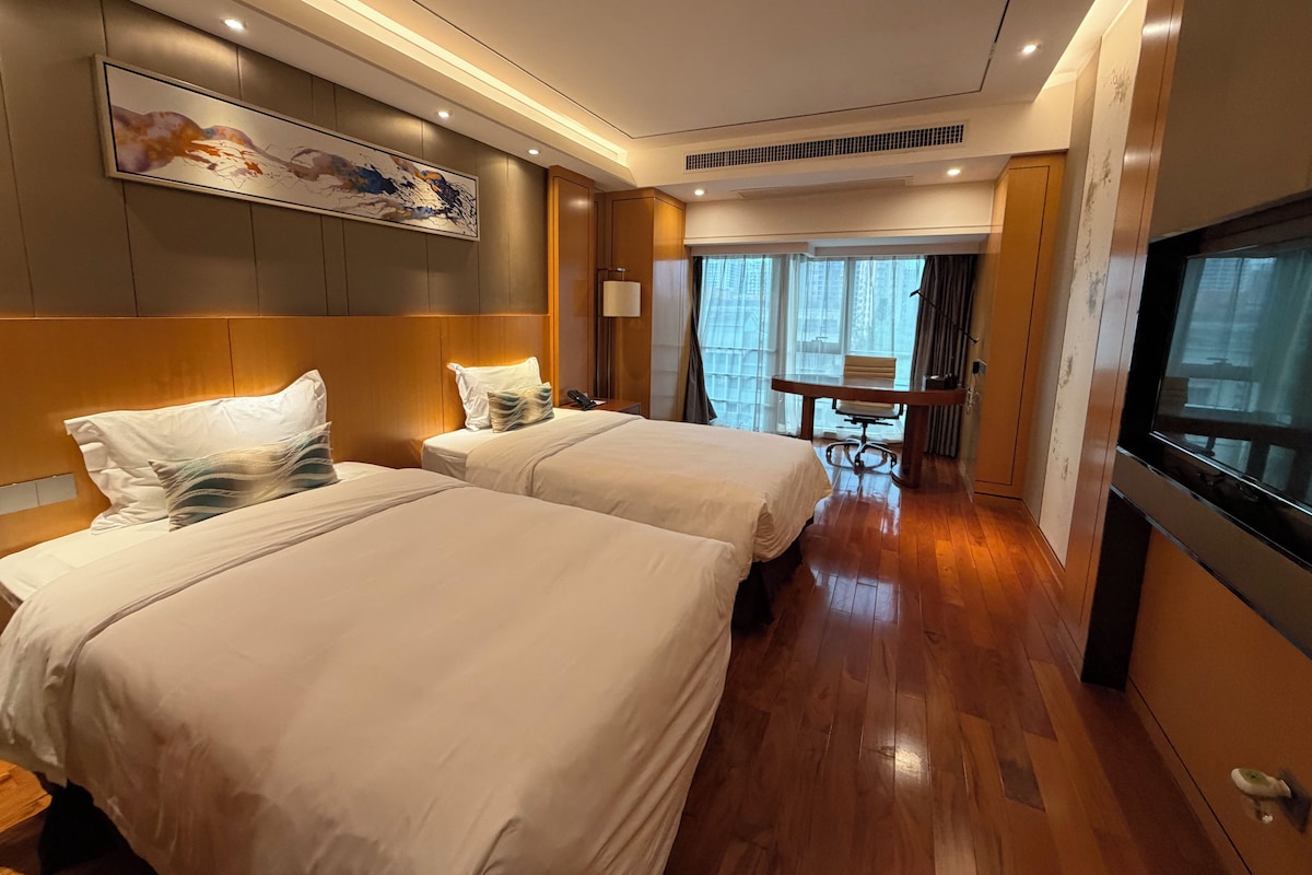 A hotel room with two beds, a desk, a chair, a TV, and a painting on the wall.
