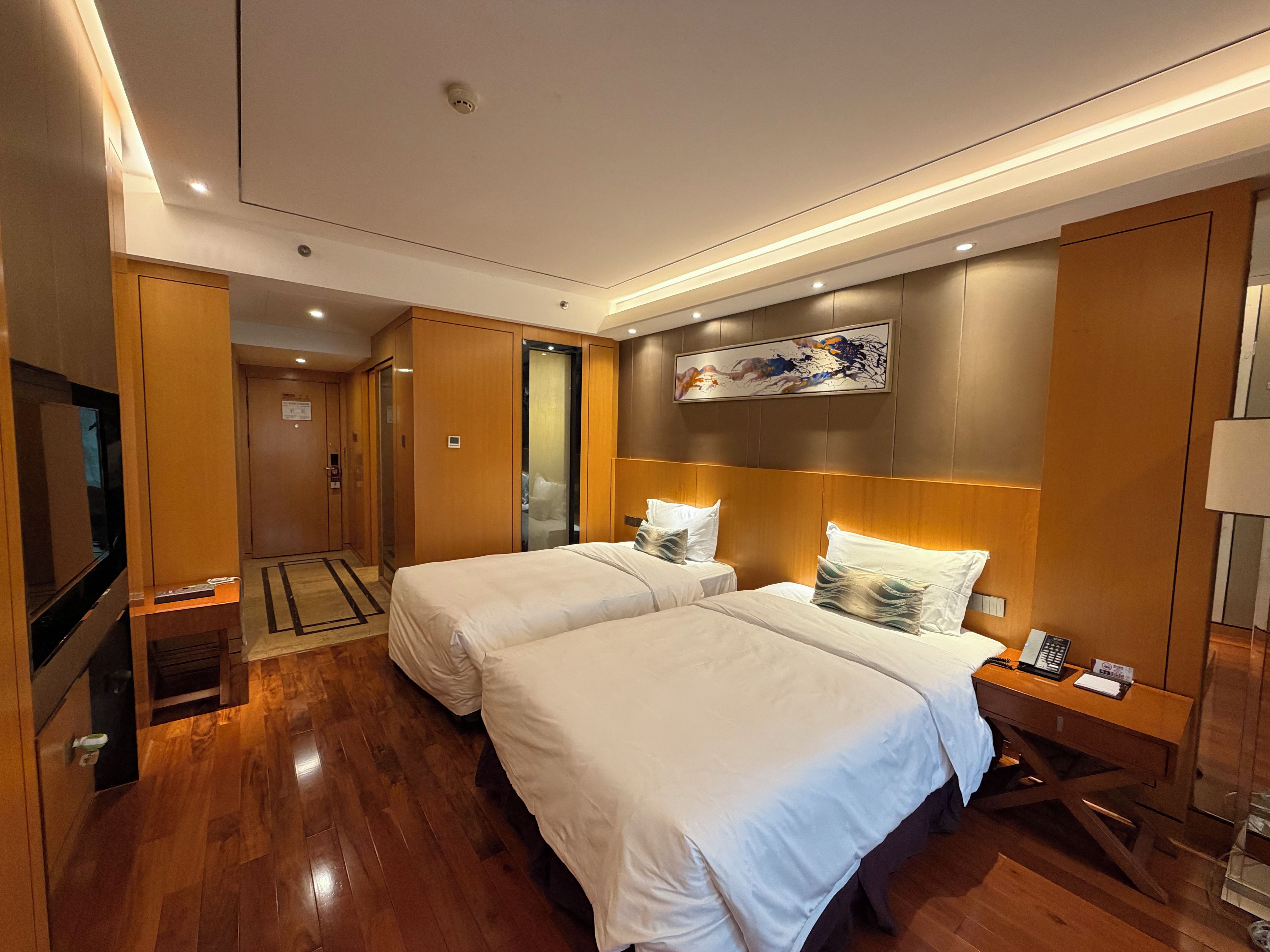 A hotel room with two beds, a desk with a telephone, a TV, and a painting on the wall.