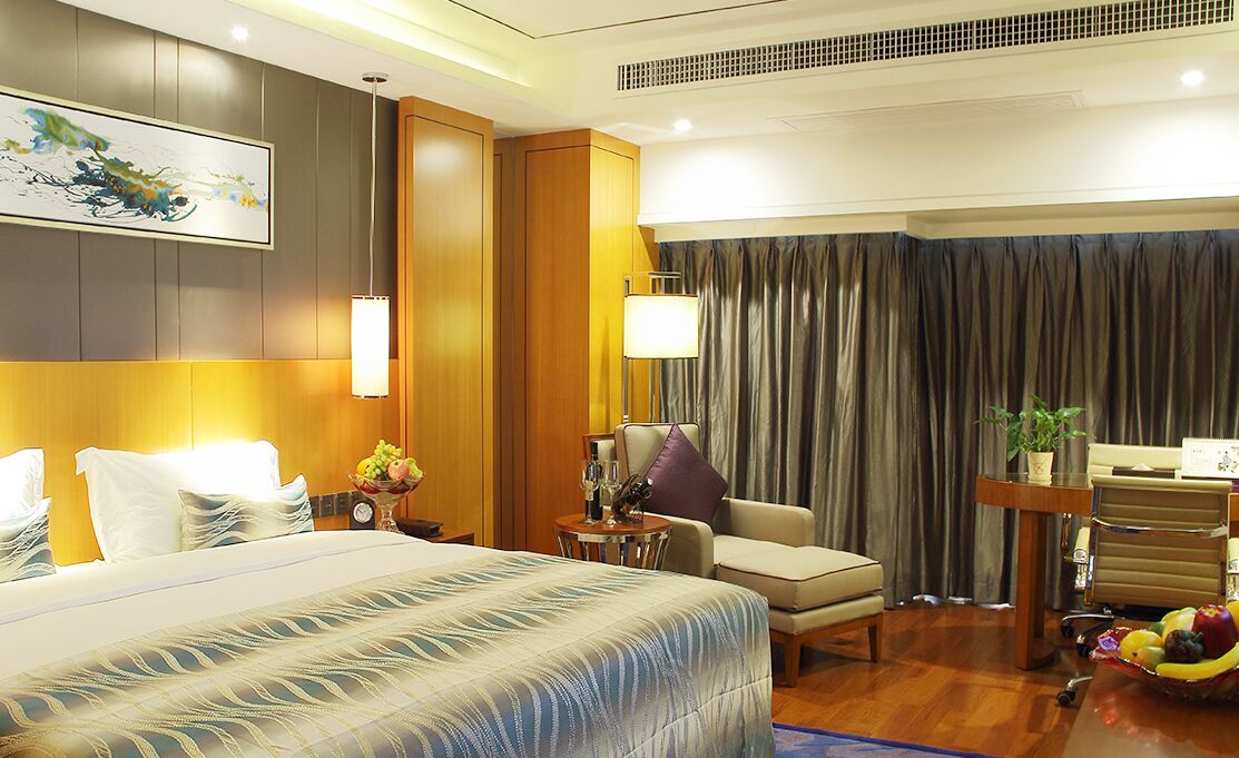 A hotel room with a large bed, a desk, a chair, a lamp, and a view of the outside.