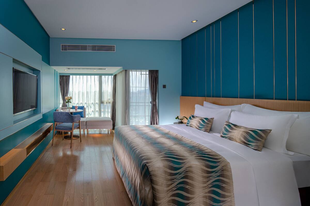 Une chambre d’hôtel avec un grand lit, un bureau avec une chaise, une télévision et une vue sur l’extérieur.