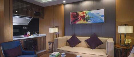 A modern living room with a sofa, armchairs, a coffee table, and a kitchen area with a microwave and sink.